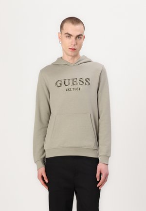 Oliwkowy hoodie z przednią kieszenią i kapturem ze sznurkiem. Zawiera logo "GUESS EST.1981" w ciemnym kolorze. Długie rękawy i teksturowany materiał.