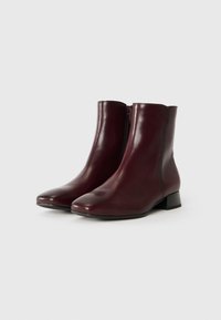 Bottes de cheville en cuir bordeaux avec un talon plat, surface lisse, bout arrondi et fermeture éclair latérale pour un enfilage facile.