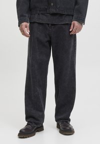 Mørk denimjakke og matchende løstsiddende bukser, begge med en falmet tekstur. Båret med mørkebrun sko med en tyk sål.
