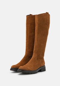 Ruskohuiset ruskeat suede-saappaat, joissa on sileä pinta, pyöreä kärki ja musta kumipohja. Niissä on hienovaraiset ompeleet ja vetosalmiakki ylhäällä.