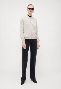Beige bombré s zipem vpředu, žebrovanými manžetami a bočními kapsami, spárovaný s černými širokými kalhotami a černými špičatými botami.