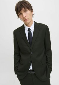 Tmavě zelený blazer s jedním knoflíkem, klopami a dvěma předními kapsami. Kombinováno s bílou košilí a černou kravatou.