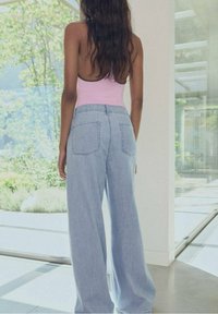 Vaaleansiniset väljät farkut korkealla vyötäröllä, joissa on kaksi takataskua ja rento istuvuus, yhdistettynä vaaleanpunaiseen tiukkaan puseroon.