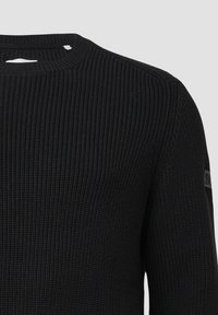 Zwart gebreid sweater met een ribbelstructuur en ronde halslijn. Beschikt over een klein logo-opprint op de mouw.