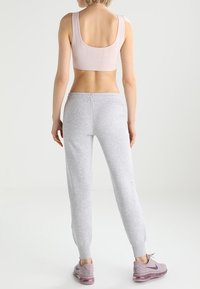 Light pink sports bra with perforated detailing, paired with gray sweatpants featuring tapered cuffs; model wearing light purple sneakers.