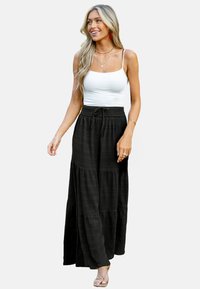Zwarte maxi rok met een gelaagd ontwerp en een gestructureerde stof. Gecombineerd met een witte tanktop, voorzien van dunne bandjes en een elastische taille.