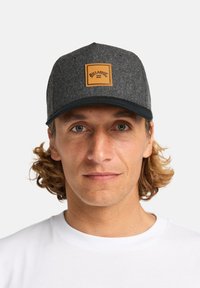 Szary wełniany kapelusz z czarnym daszkiem, z prostokątną brązową skórzaną łatą z tekstem. Casualowy design, idealny do noszenia na zewnątrz.