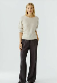 Helles beige gestricktes Sweatshirt mit weitem Ausschnitt und Fronttaschen, kombiniert mit dunkelgrauen, taillierten Hosen mit gerader Schnittführung und präzisen Nähten.