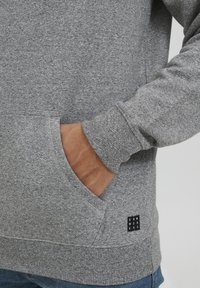 Grijze hoodie van zacht, textuurstof met een buidelzak en geribde boorden. Klein zwart label geplaatst op de onderste zoom.