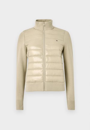 Beżowa pikowana kurtka z wysokim kołnierzem, z błyszczącym przednim panelem oraz miękkimi, dzianinowymi rękawami i mankietami, zapinana na zamek, z małym detalem z logo.