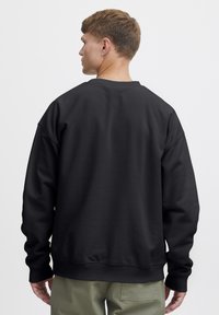 Sudadera negra con un corte relajado, puños y dobladillo acanalados. Textura de tela suave, cuello redondo y diseño simple.