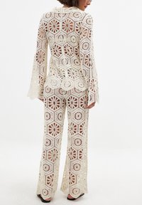 Tuta all'uncinetto color crema, con motivi floreali e geometrici, maniche larghe, gambe a pantalone svasate e design con schiena scoperta.