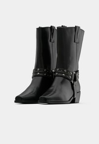 Μαύρα δερμάτινα μπότακια μέχρι τον αστράγαλο με λείο φινίρισμα, ρυθμιζόμενους ιμά ντες με ασημένια καρφιά, μυτερές μύτες και χαμηλό τακούνι με στοίβαξη.