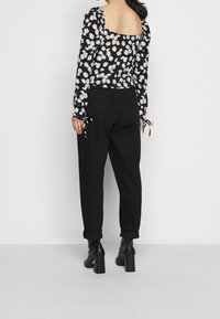 Kvinna i svarta uppvikta byxor, svarta klackade ankelboots och en svart långärmad topp med vita prästkragar och öppen rygg.