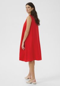Röd ärmlös klänning med en lös A-linje design och texturerad tyg. Kombinerad med ljusa slingback-skor med låg klack.