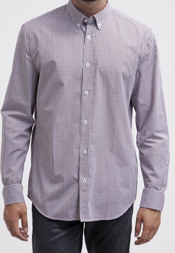 Hombre vistiendo una camisa de cuadros pequeña en púrpura y blanco, de manga larga y abotonada, con cuello y puños, combinada con pantalones oscuros.