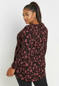 Blusa nera floreale con un motivo di fiori rosa e rossi, maniche lunghe, vita arricciata e silhouette leggermente svasata.