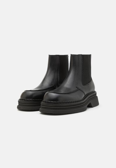 Bottines en cuir noir avec des panneaux latéraux élastiques, une semelle plateforme épaisse et des coutures décoratives le long des bords.