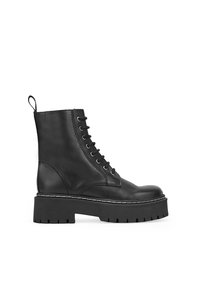 Botas de cuero negro hasta el tobillo con una suela de plataforma gruesa, punta redonda y diseño con cordones en la parte delantera. Cuenta con un tirador y costuras en blanco que contrastan.