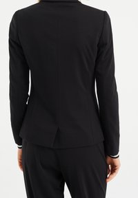 Svart skräddarsydd kavaj med smal passform, med hakkrage och slits bak. Tillverkad i mjukt tyg med långa ärmar och strukturerad design.