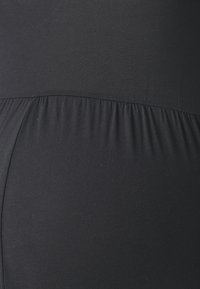 Black stretchy fabric with a smooth texture, featuring a gathered waistband and a seamless design that contours the body.