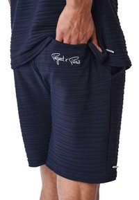 Pantalones cortos azul marino confeccionados en tejido texturizado, con un bolsillo lateral que presenta el logo "Project x Paris" y detalles en plata para añadir elegancia.