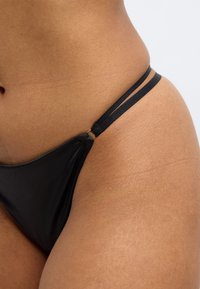 Μαύρο κάτω μέρος μπικίνι με μινιμαλιστικό σχεδιασμό, διπλές λεπτές τιράντες και λεία υφή, με κοντινή λήψη του υφάσματος.
