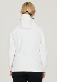 Vit mjukskaljacka med en åtsittande design, huva, justerbara snörningar och svarta detaljer vid ärmar och nederkant.