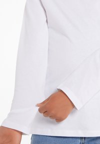 Weißes Langarmshirt mit rundem Halsausschnitt; hat einen geraden Saum und Manschetten; aus glattem Baumwollstoff. Hand verstellbare Ärmel.
