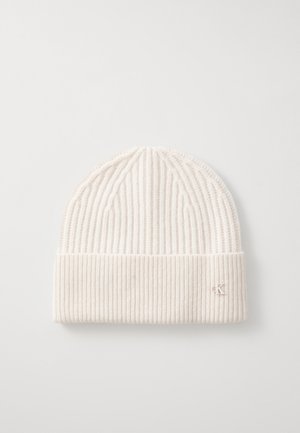 Knit beanie in light beige with ribbed texture. Features a folded brim and a small embroidered logo on the side. Soft wool material.