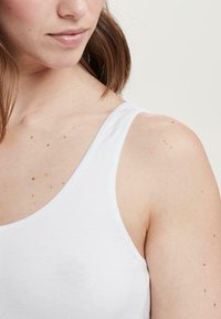 Hvid tanktop lavet af bomuld, med spaghetti-stropper og en rund halsudskæring. Glat tekstur med minimal dekoration, der fremhæver et enkelt design.
