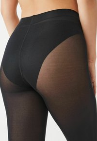 Svarte leggings med høj talje, der har et semi-gennemsigtigt panel på ydersiden af låret, glat tekstur og tætsiddende design.