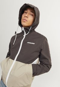 Windbreaker in dark brown and beige, featuring a zip front, adjustable hood, and elastic cuffs; logo on chest, two front pockets.