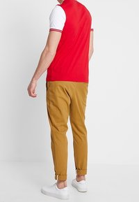 Camisa polo roja y blanca de manga corta, combinada con pantalones tapered en color beige. Zapatillas blancas completan el conjunto.