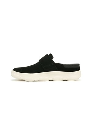 Chaussure en suède noir à enfiler avec une semelle épaisse et ondulée blanche. Elle possède une large sangle sur le dessus et une section de talon lisse.
