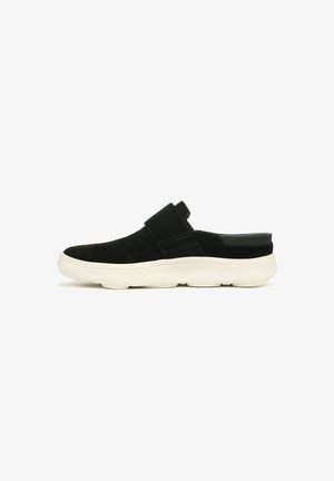 Chaussure en suède noir à enfiler avec une semelle épaisse et ondulée blanche. Elle possède une large sangle sur le dessus et une section de talon lisse.