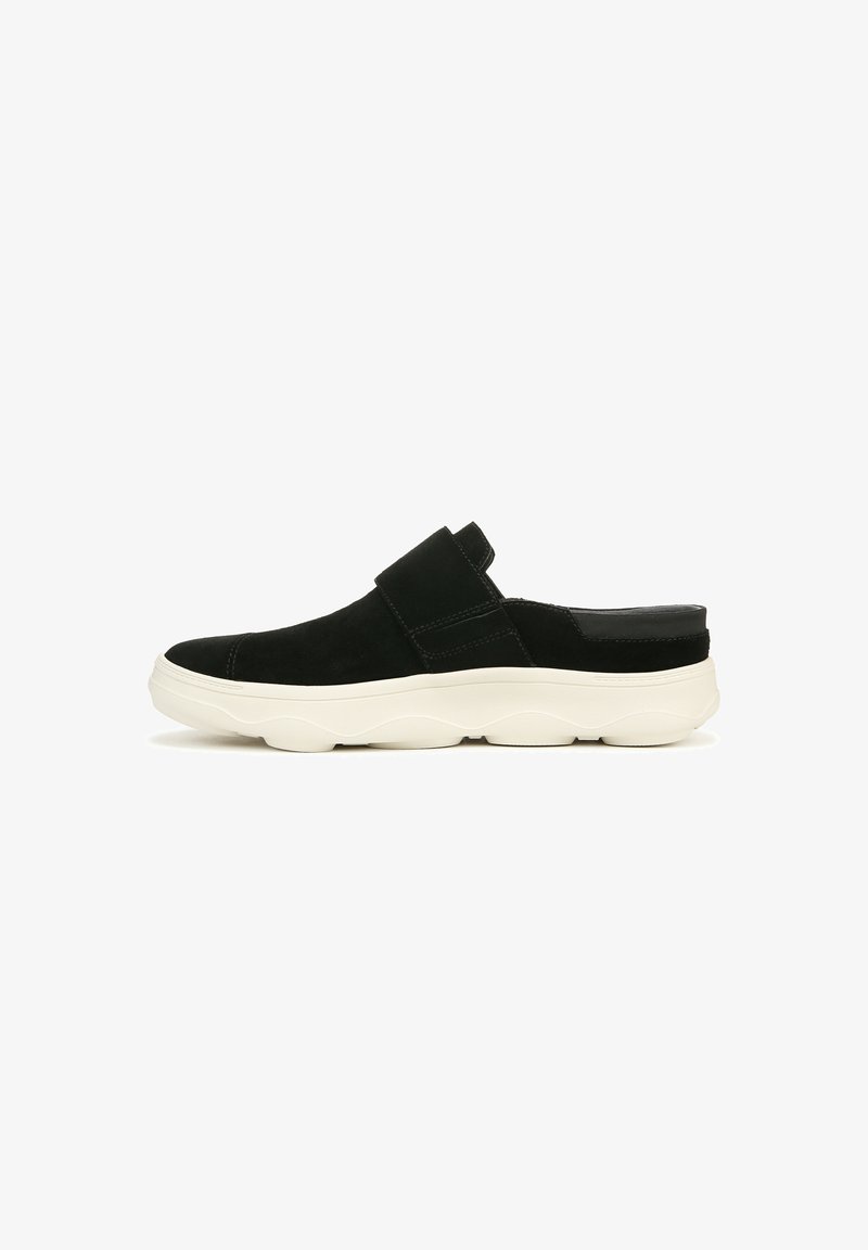 Chaussure en suède noir à enfiler avec une semelle épaisse et ondulée blanche. Elle possède une large sangle sur le dessus et une section de talon lisse.