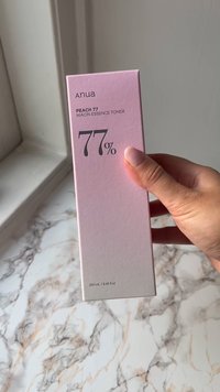 Roze en witte tonerdoos met "PEACH 77" en "77%" in het zwart gedrukt. Bevat 250 ml niacin-essence toner, met een gladde textuur.