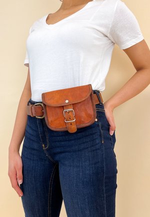 Personne portant un t-shirt blanc et un jean bleu foncé avec une ceinture-sac en cuir marron attachée à la taille.