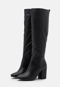 Botas negras hasta la rodilla con textura de cocodrilo. Tienen una puntera afilada y un tacón cuadrado. Forro interior suave y detalles de costura.