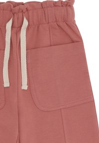Weiche rosa Stoffhose mit elastischem Bund, großen vorderen aufgesetzten Taschen und hängenden weißen Zugbändern.