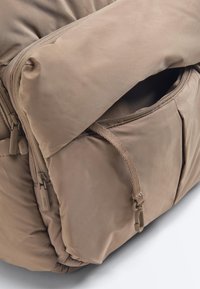 Beiger gepolsterter Stoffrucksack mit mehreren Reißverschlussfächern, Nahaufnahme der offenen Fronttasche und Kordeldetail.