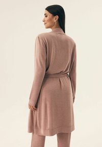 Długi, rozpinany kardigan z miękkiego różowego materiału. Posiada prążkowaną teksturę, paskiem w talii oraz długimi rękawami. Minimalistyczny design, bez wzorów.