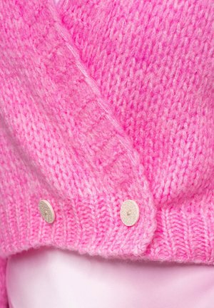 Roze gebreide trui met een gestructureerd patroon en twee crèmekleurige knopen. Heeft een V-hals en een geribbelde zoom. Zachte, tactile stof.