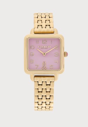 Reloj cuadrado de oro con esfera rosa, números dorados, logo de Coach New York, cinta rosa a las seis y correa de pulsera de oro enlazada.