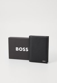 Čierna kožená peňaženka s textúrovaným povrchom, vystavená vedľa čiernej škatuľky so bielym logom "BOSS" viditeľne na prednej strane.