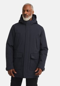 Parka bleu marine avec capuche, deux poches poitrine et deux poches avant. Texture lisse avec un design moderne et fonctionnel.