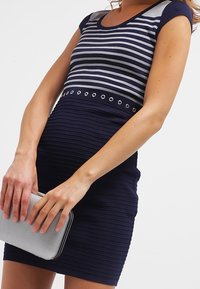 Robe à rayures bleu marine et argent avec manches courtes, coupe ajustée texturée, accents circulaires argentés à la taille, et sac pochette argenté.