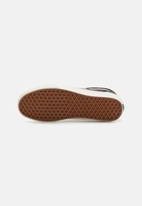Semelle plate de basket avec un motif gaufré marron et une semelle intermédiaire blanche sur un fond clair uni.
