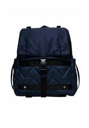 Tmavě modrý prošívaný batoh s klopou na zapínání, černým páskem se sponou, bočními kapsami a knoflíkovými detaily na bílém pozadí.